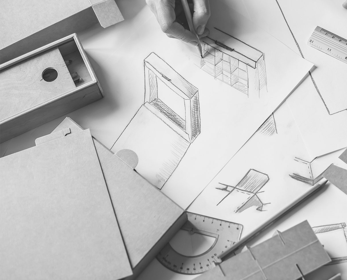 Hands drawing a structural packaging sketch beside folding-box material samples