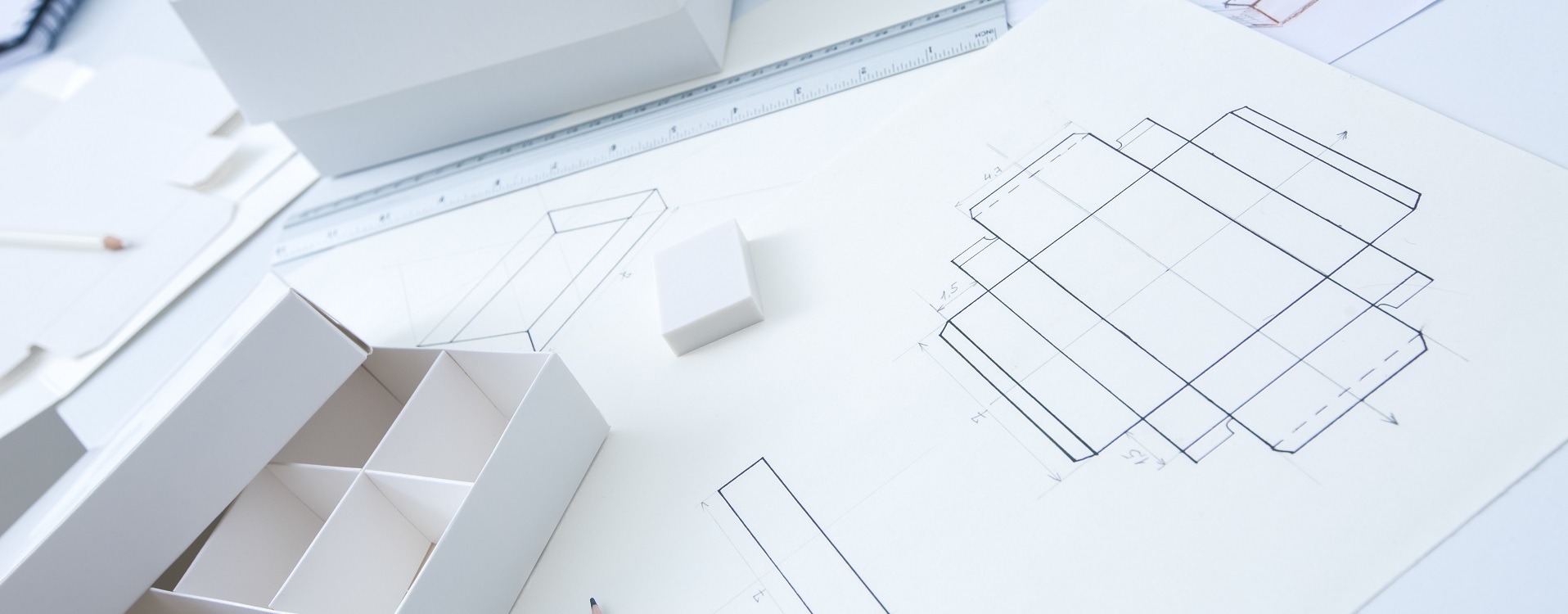 White compartment box model, ruler and packaging dieline drawings on a worktable